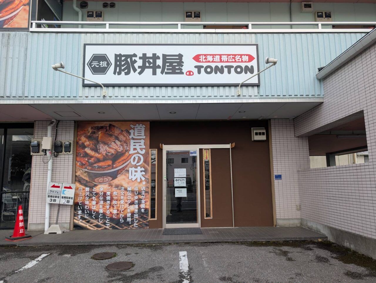 豚丼屋トントンの店舗の外観(前面)。明るい水色の壁の建物の1階にあり、店の看板や大きなタペストリーが掲出されています。